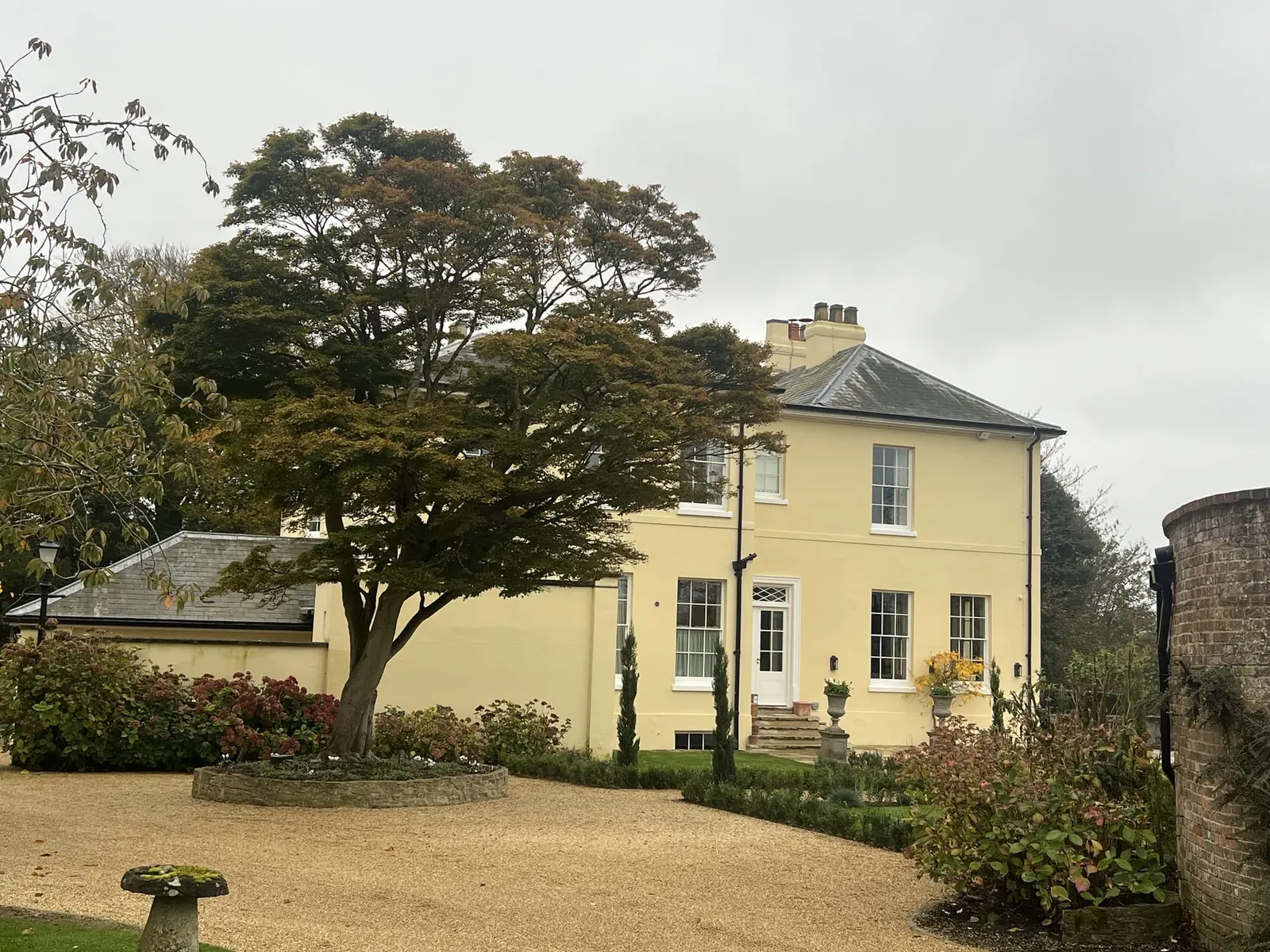 The house seen past a mature cedar, gravel sweep and clipped planting in front.