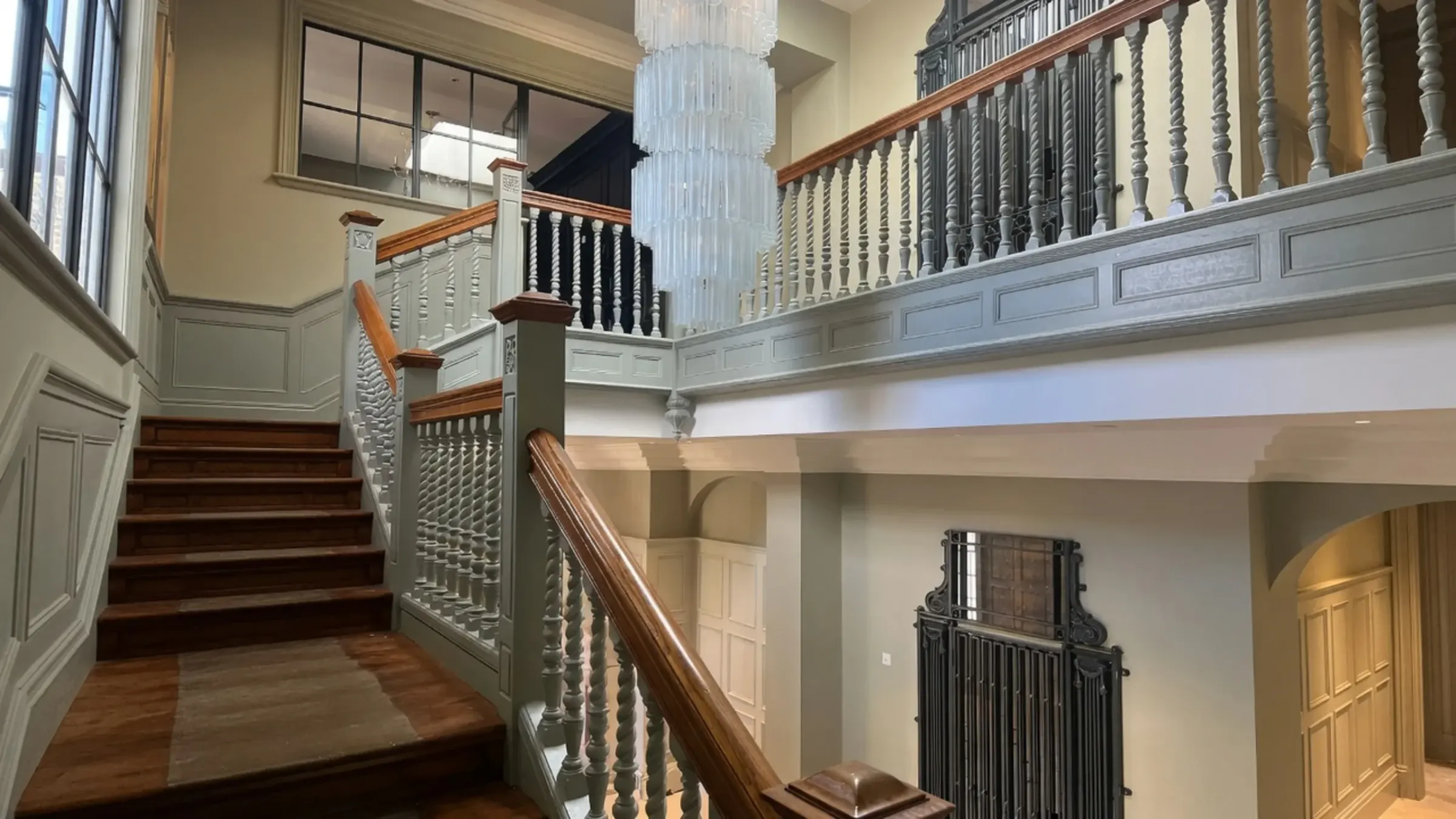 A restored staircase hall with painted panelling, timber handrails and a tiered glass chandelier.